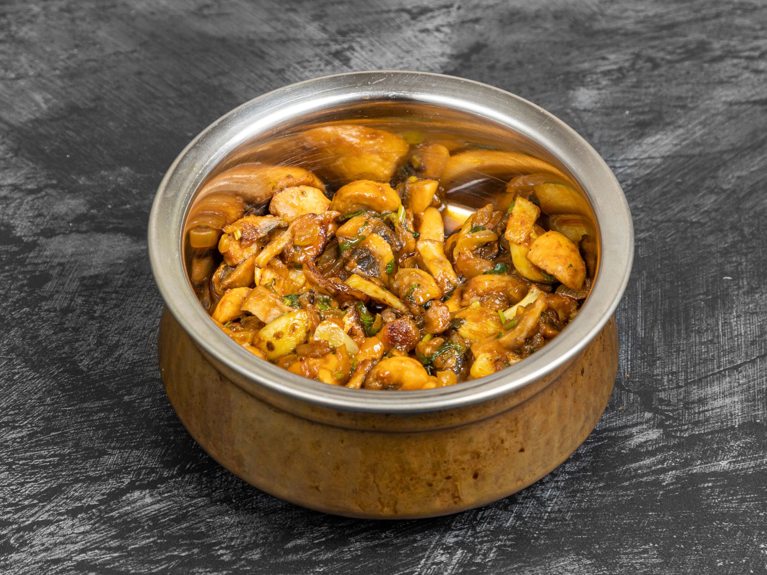 Mushroom bhaji with visible slices of onion and green herbs in a decorative copper serving bowl