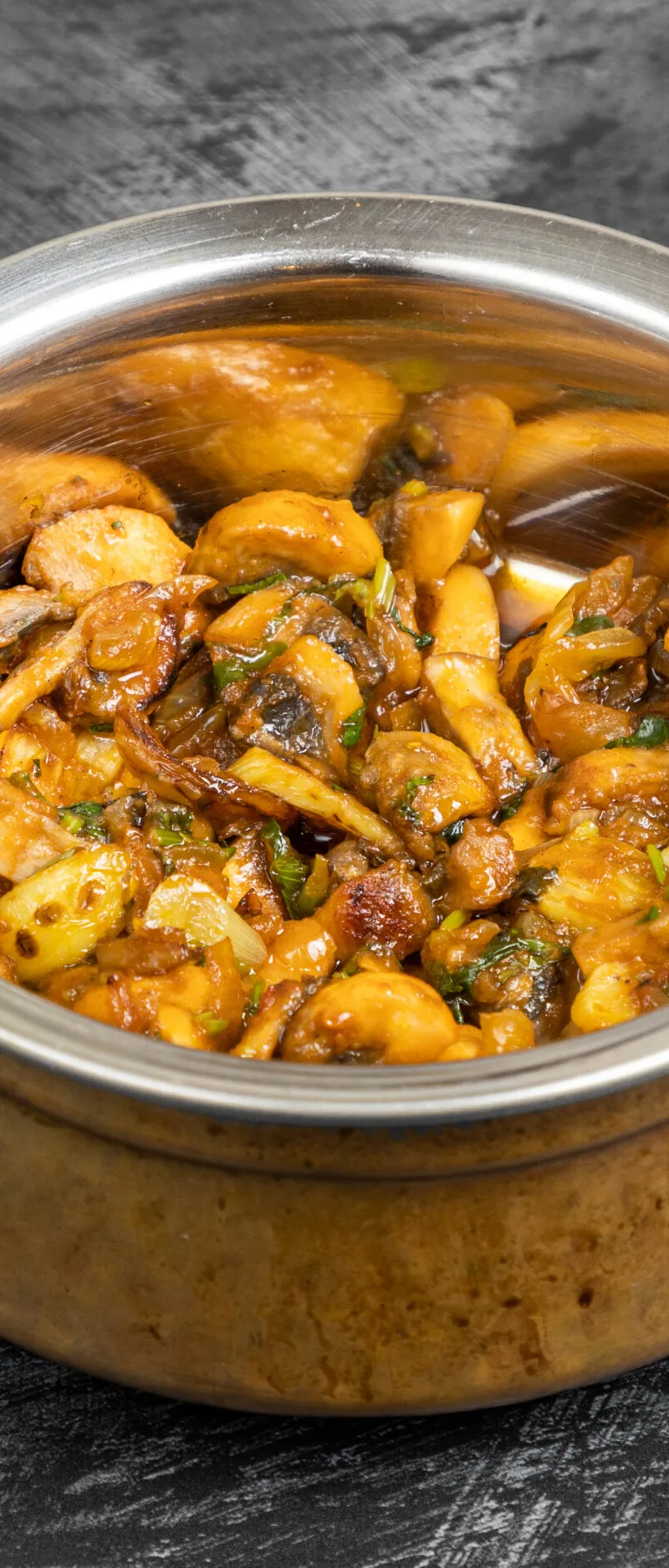 Mushroom bhaji with visible slices of onion and green herbs in a decorative copper serving bowl