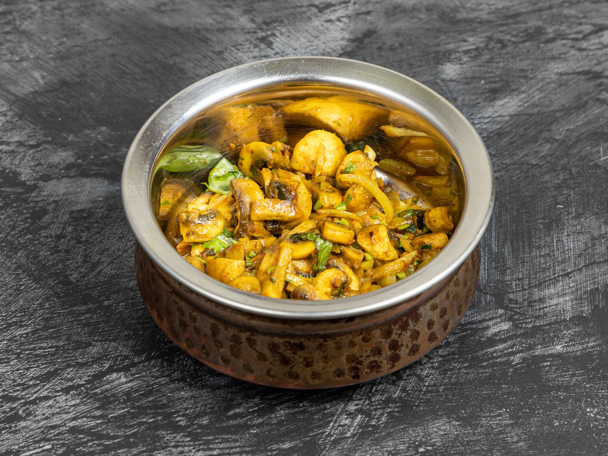 Mushroom and potato curry with green herbs, served in a hammered copper and steel karahi dish.