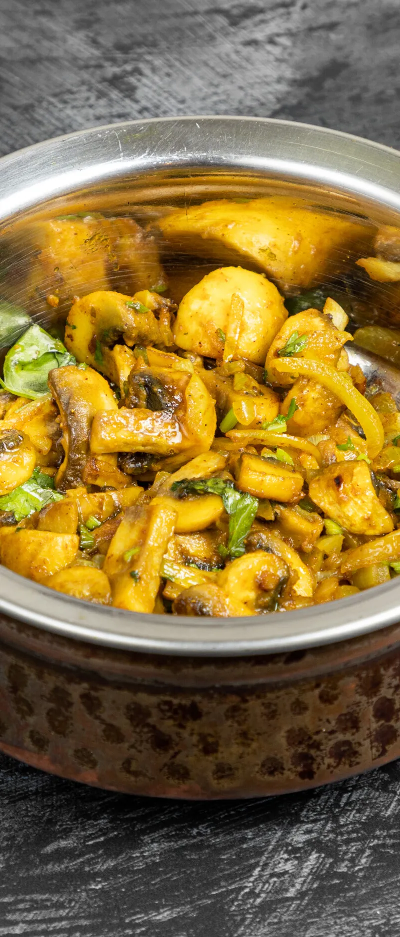 Mushroom and potato curry with green herbs, served in a hammered copper and steel karahi dish.