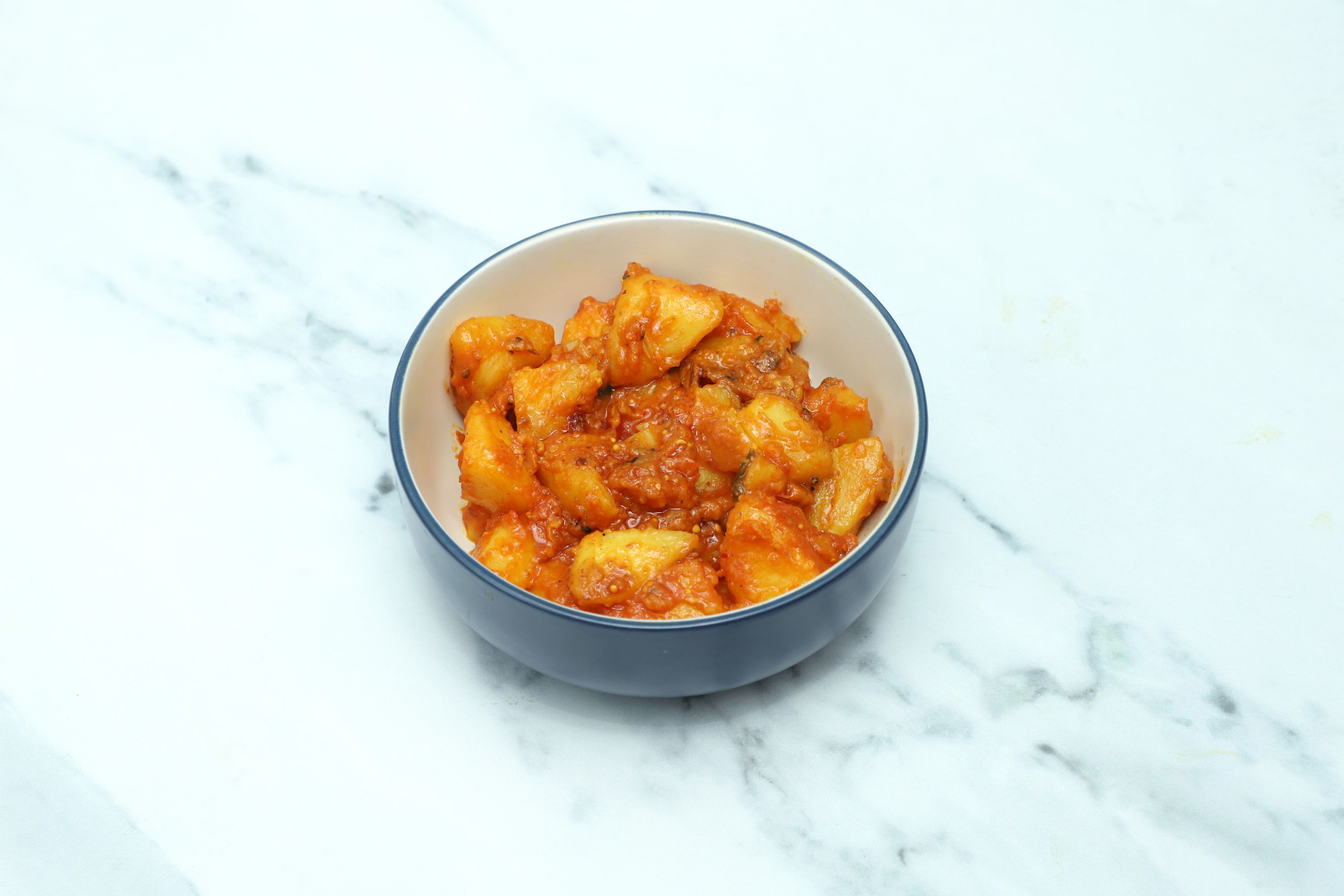 A blue and white bowl filled with Aloo ki Sabzi, potato chunks in a red-orange sauce.