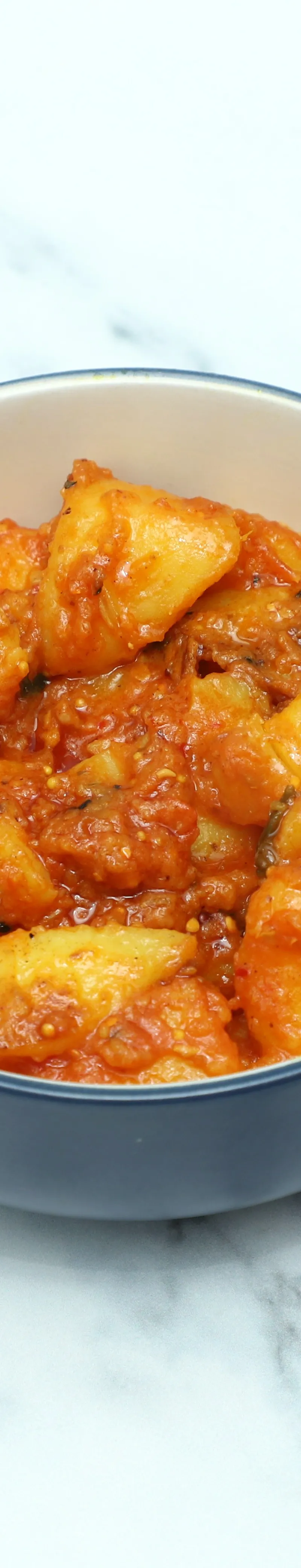A blue and white bowl filled with Aloo ki Sabzi, potato chunks in a red-orange sauce.