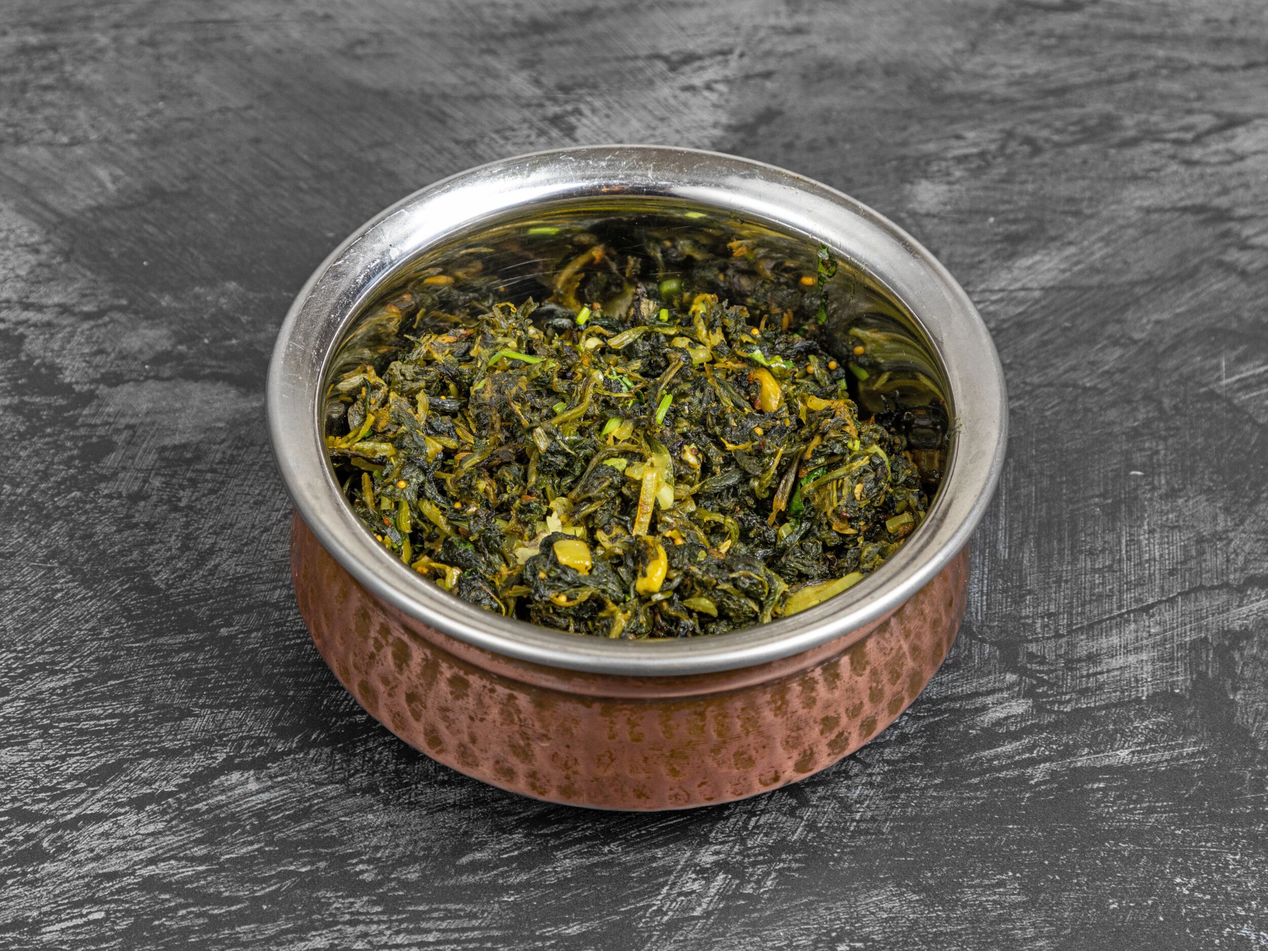 Spinach curry, dark green with lighter flecks, served in a hammered copper karahi bowl.