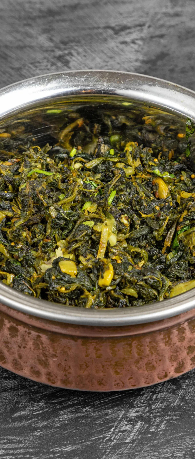 Spinach curry, dark green with lighter flecks, served in a hammered copper karahi bowl.