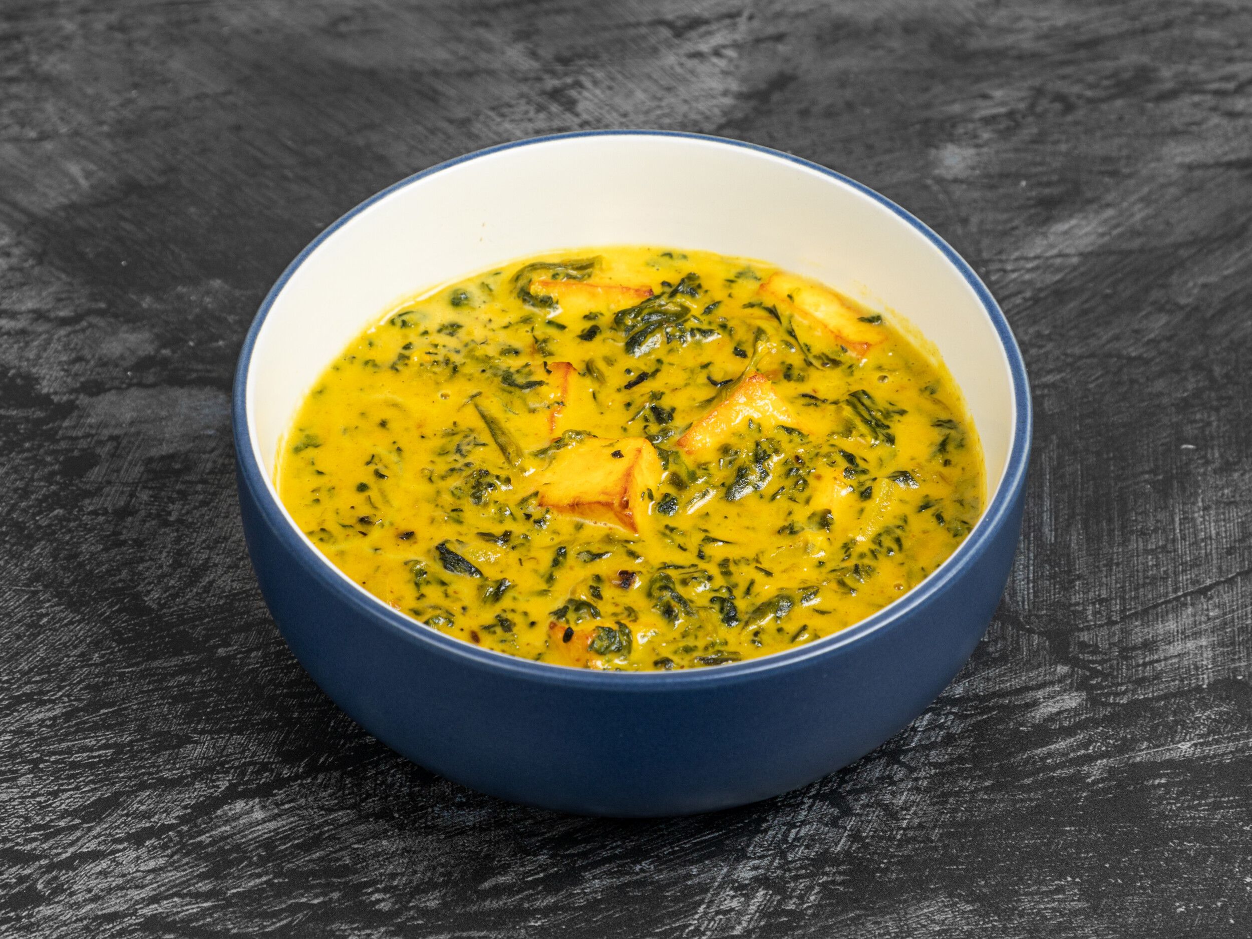 A close-up shot of palak paneer in a blue and white bowl on a black surface.