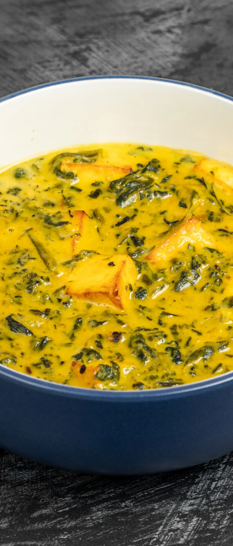 A close-up shot of palak paneer in a blue and white bowl on a black surface.