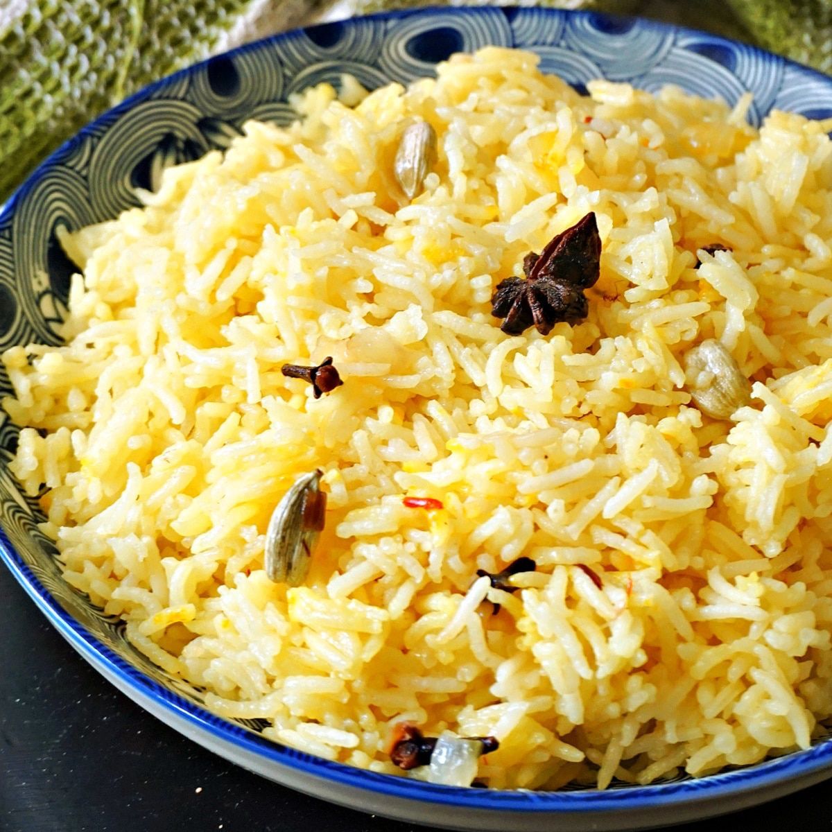Basmati rice cooked with whole spices, including star anise, cardamom, and cloves, in a blue and white patterned bowl.