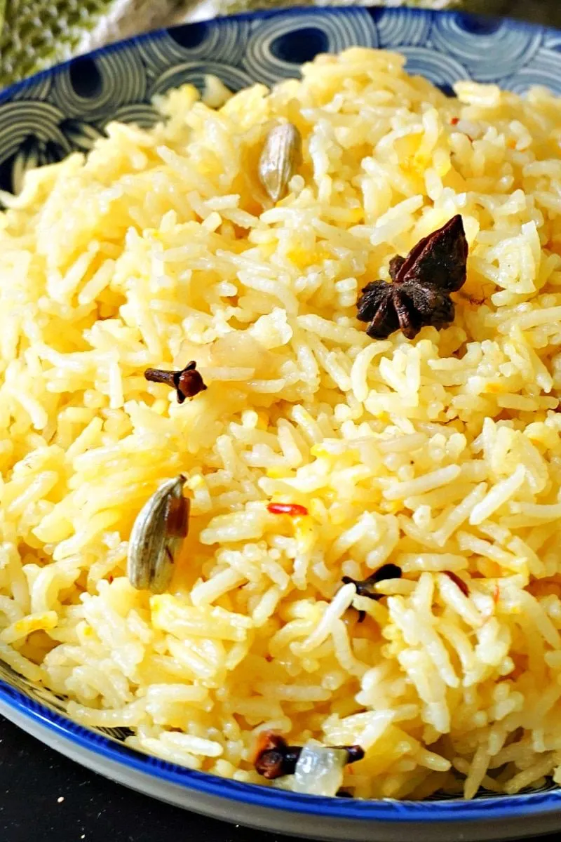 Basmati rice cooked with whole spices, including star anise, cardamom, and cloves, in a blue and white patterned bowl.