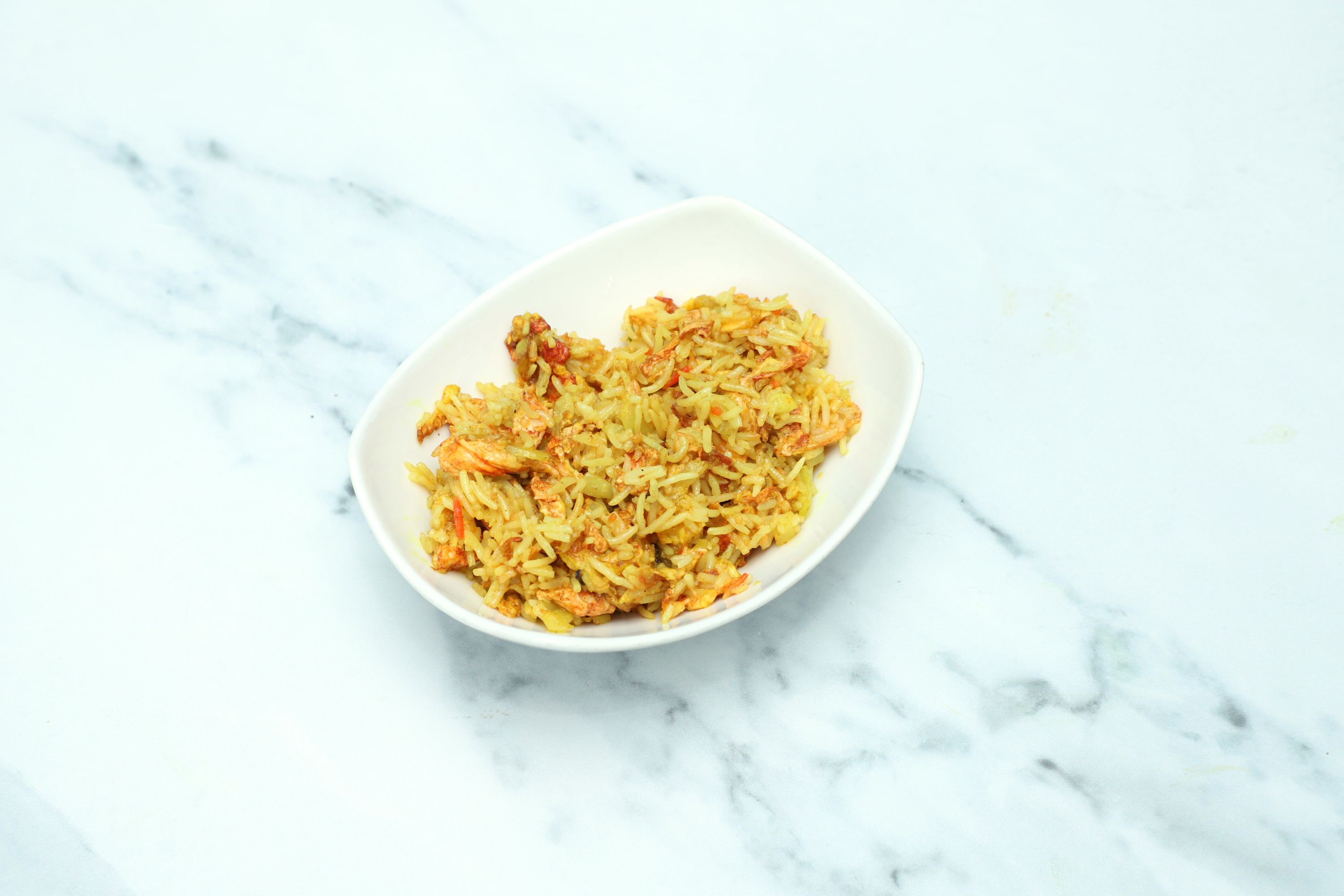 Masala rice with pieces of prawn and scrambled egg in a white rectangular bowl on a marble surface