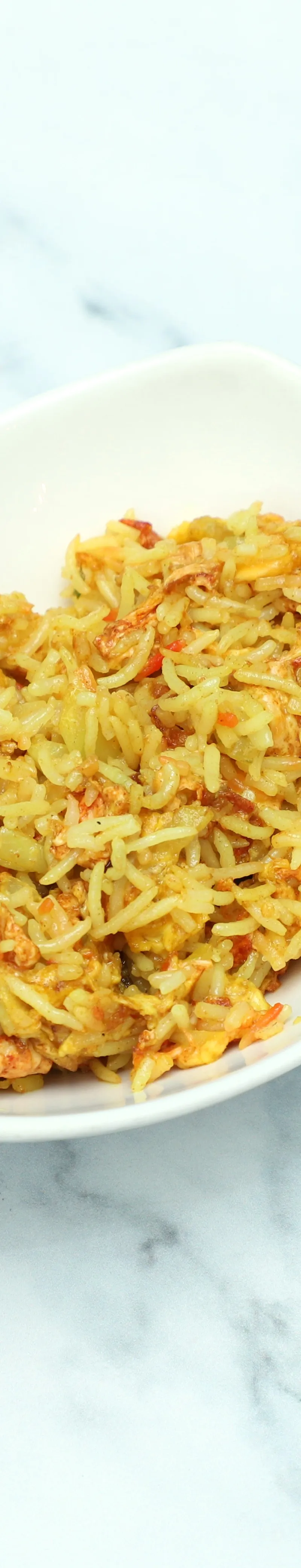 Masala rice with pieces of prawn and scrambled egg in a white rectangular bowl on a marble surface