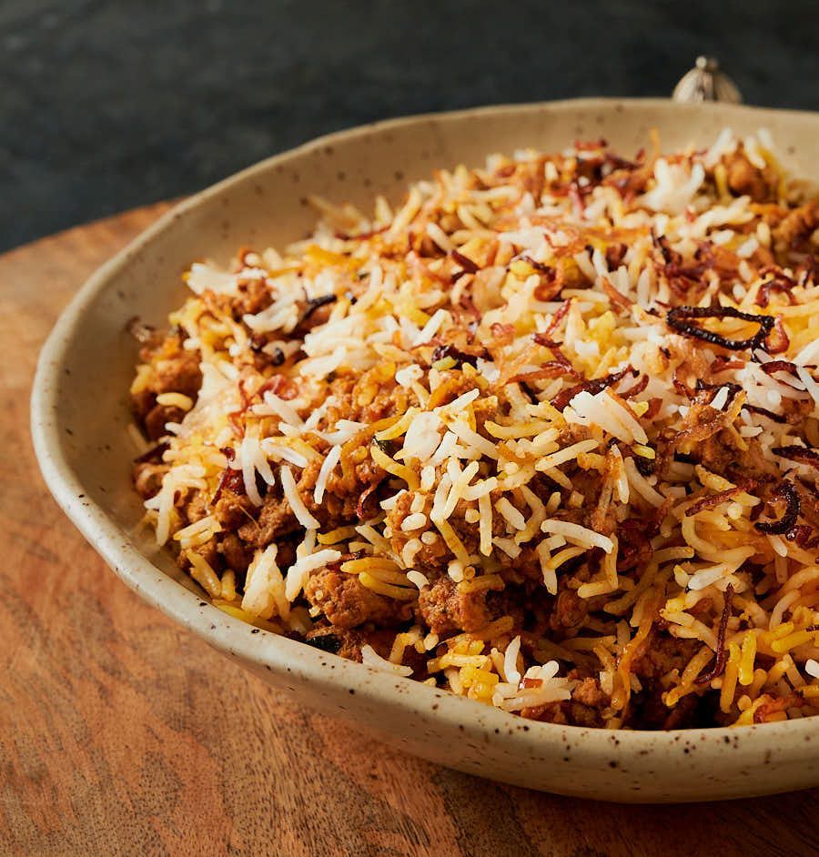 Close-up of a stoneware bowl filled with minced meat biryani topped with crispy fried onions.