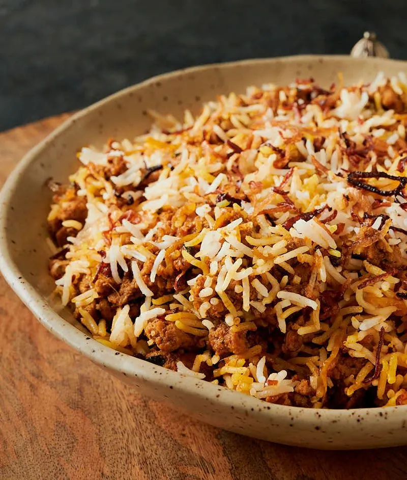 Close-up of a stoneware bowl filled with minced meat biryani topped with crispy fried onions.