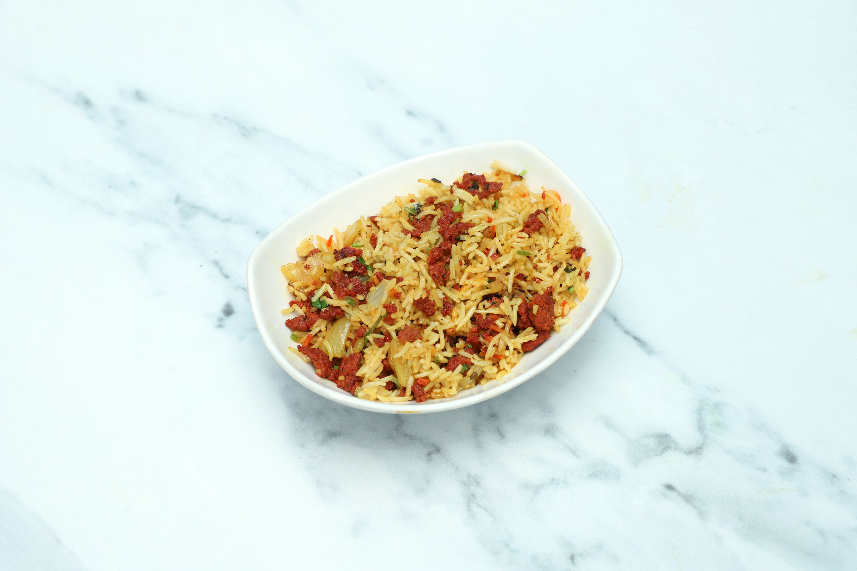 Top-down view of rice pilaf with minced lamb and chopped vegetables in a white ceramic dish