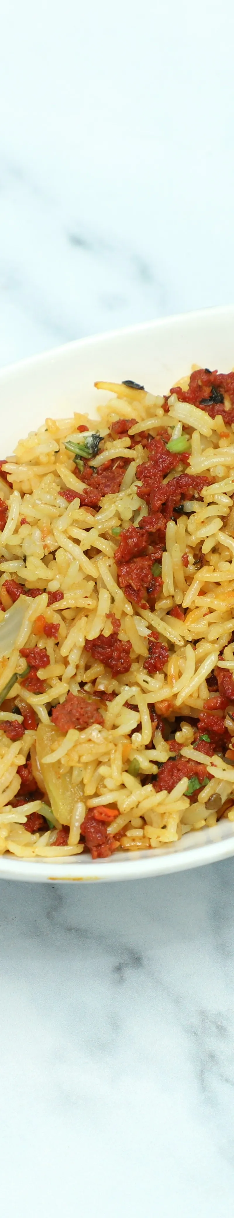 Top-down view of rice pilaf with minced lamb and chopped vegetables in a white ceramic dish