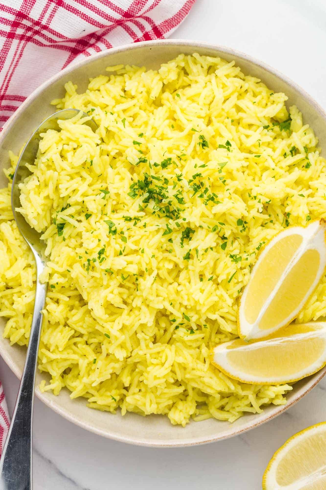 Bright yellow rice in a light-coloured bowl, garnished with fresh chopped herbs and lemon slices.
