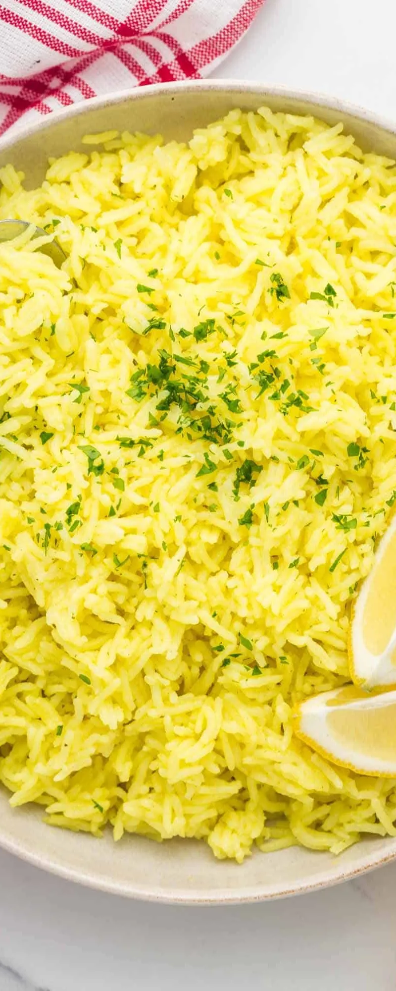 Bright yellow rice in a light-coloured bowl, garnished with fresh chopped herbs and lemon slices.