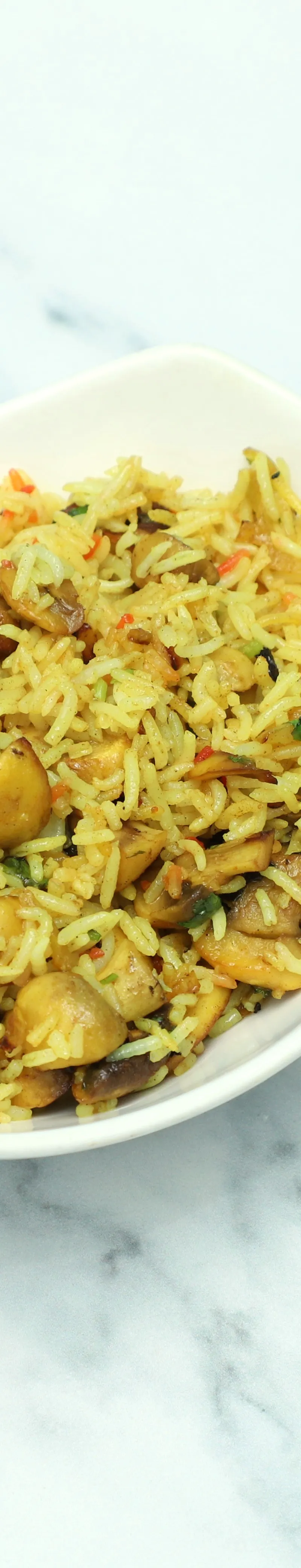 Mushroom pilau in a white, elongated bowl on a light marble surface. Rice is yellow with visible mushrooms.