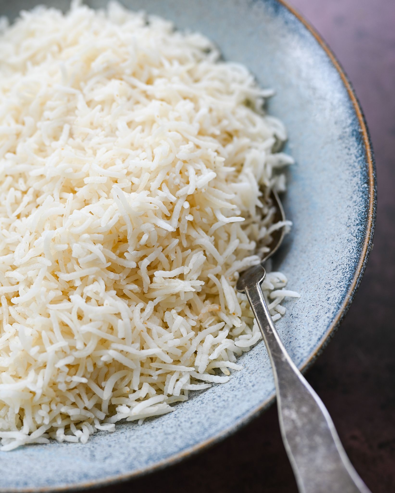 Close-up of fluffy white basmati rice in a light blue textured bowl with a silver spoon