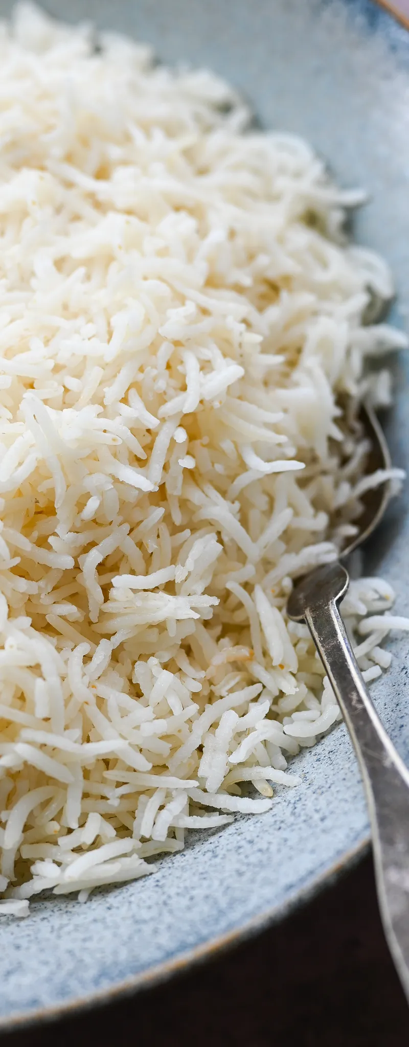 Close-up of fluffy white basmati rice in a light blue textured bowl with a silver spoon