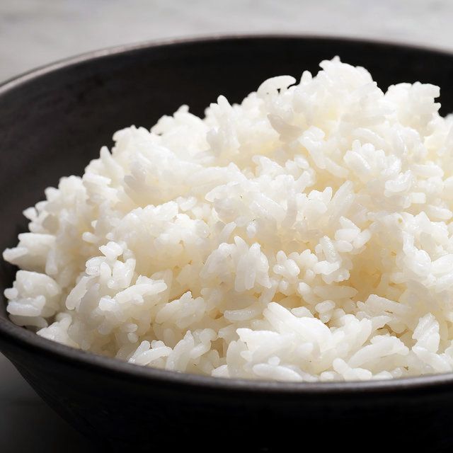 A close-up shot of a dark bowl filled with fluffy, white basmati rice, ready to serve.