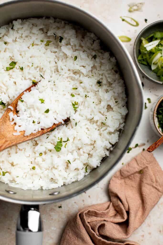 Fluffy white basmati rice with green coriander in a silver pot with a wooden spoon