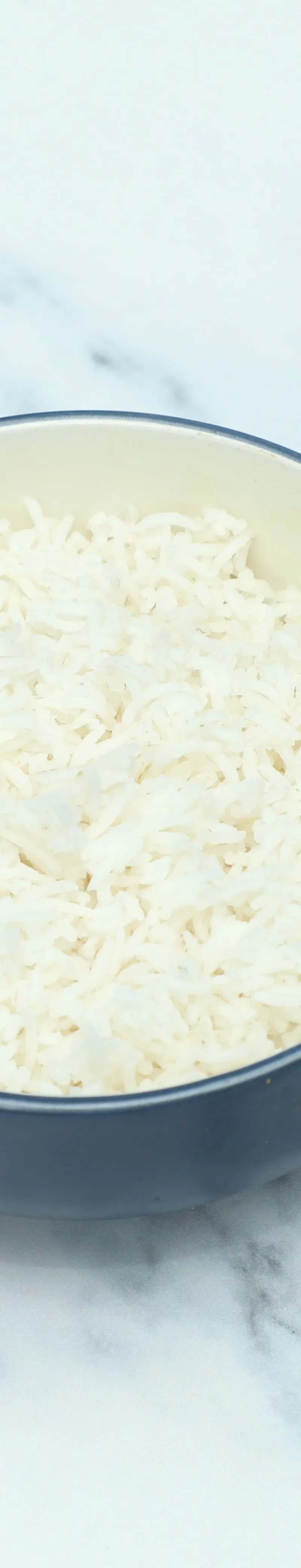 A round, dark blue and cream bowl filled with fluffy white basmati rice on a white marble surface.
