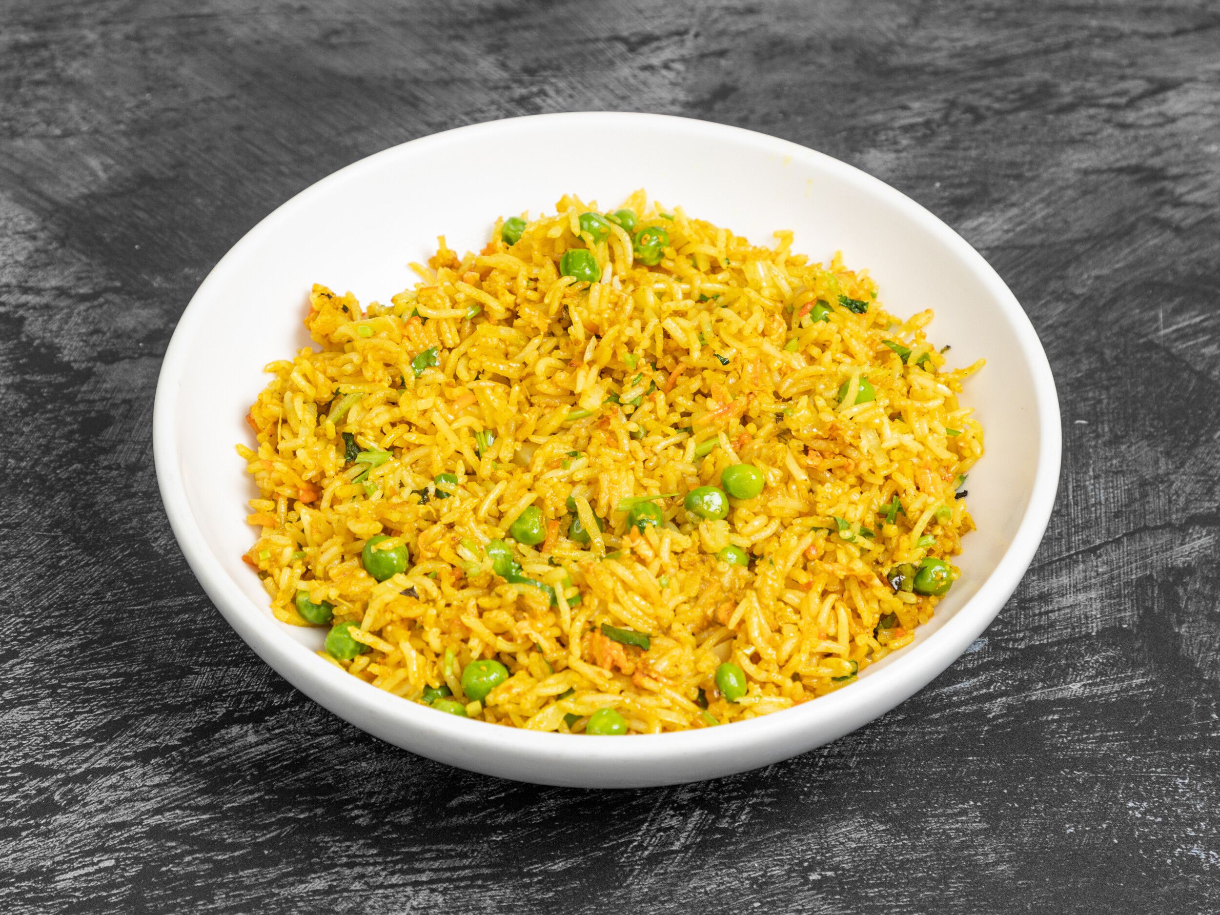 Close-up of vibrant yellow pea pulao rice in a white bowl on a dark grey surface.