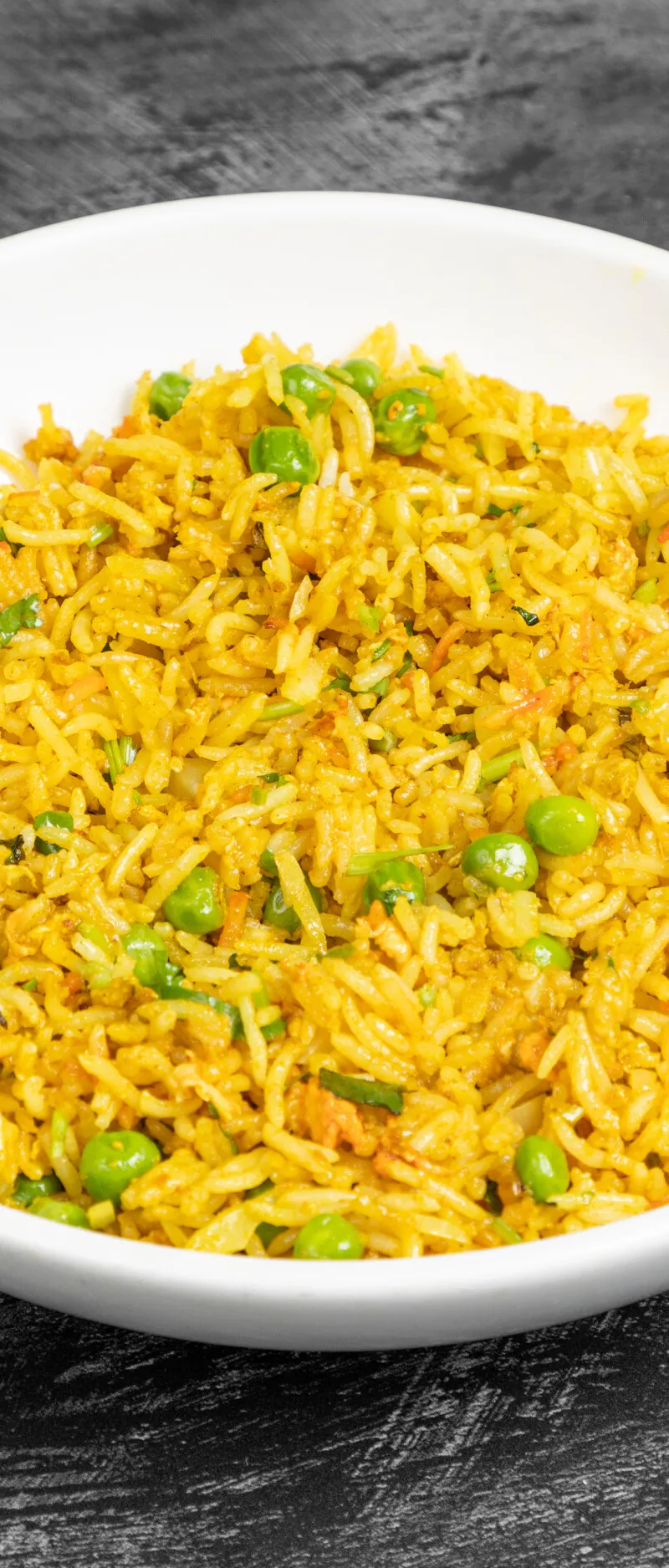 Close-up of vibrant yellow pea pulao rice in a white bowl on a dark grey surface.