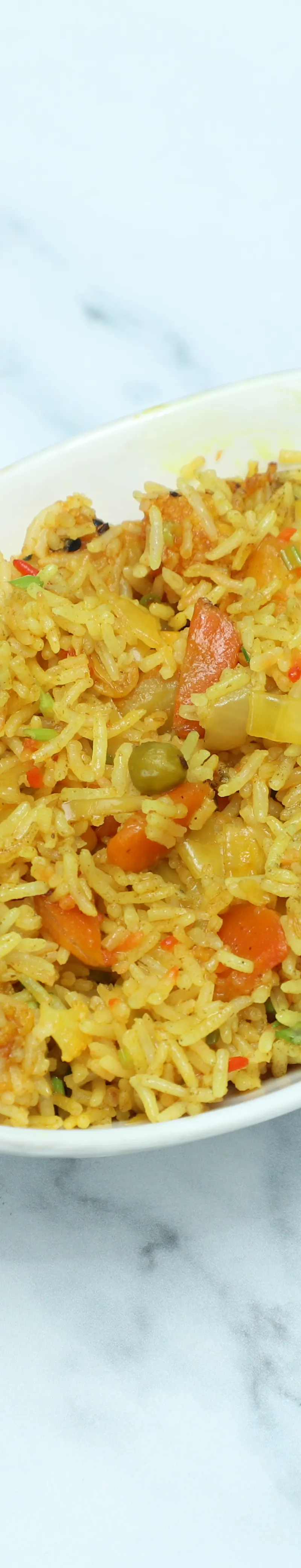 A white oval bowl filled with colourful vegetable biryani rice on a white marble surface