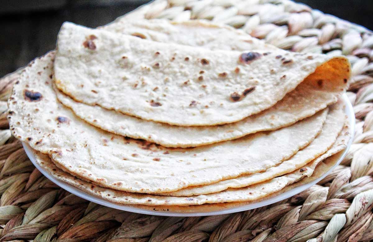 A stack of light brown flatbreads, possibly rotis or chapatis, on a white plate.