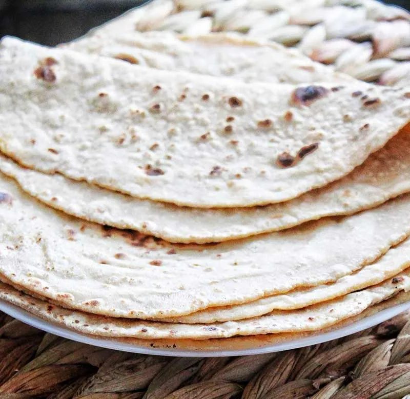 A stack of light brown flatbreads, possibly rotis or chapatis, on a white plate.
