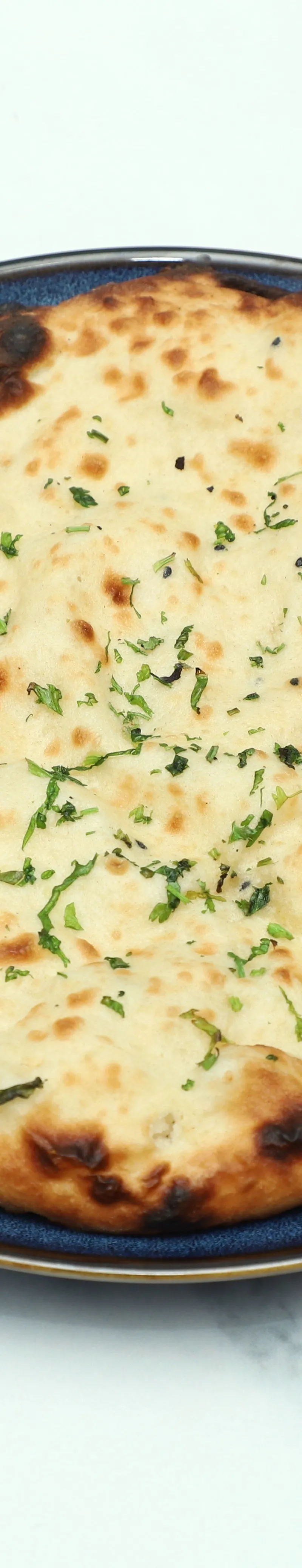 A round naan bread topped with fresh green herbs and sesame seeds on a blue plate.