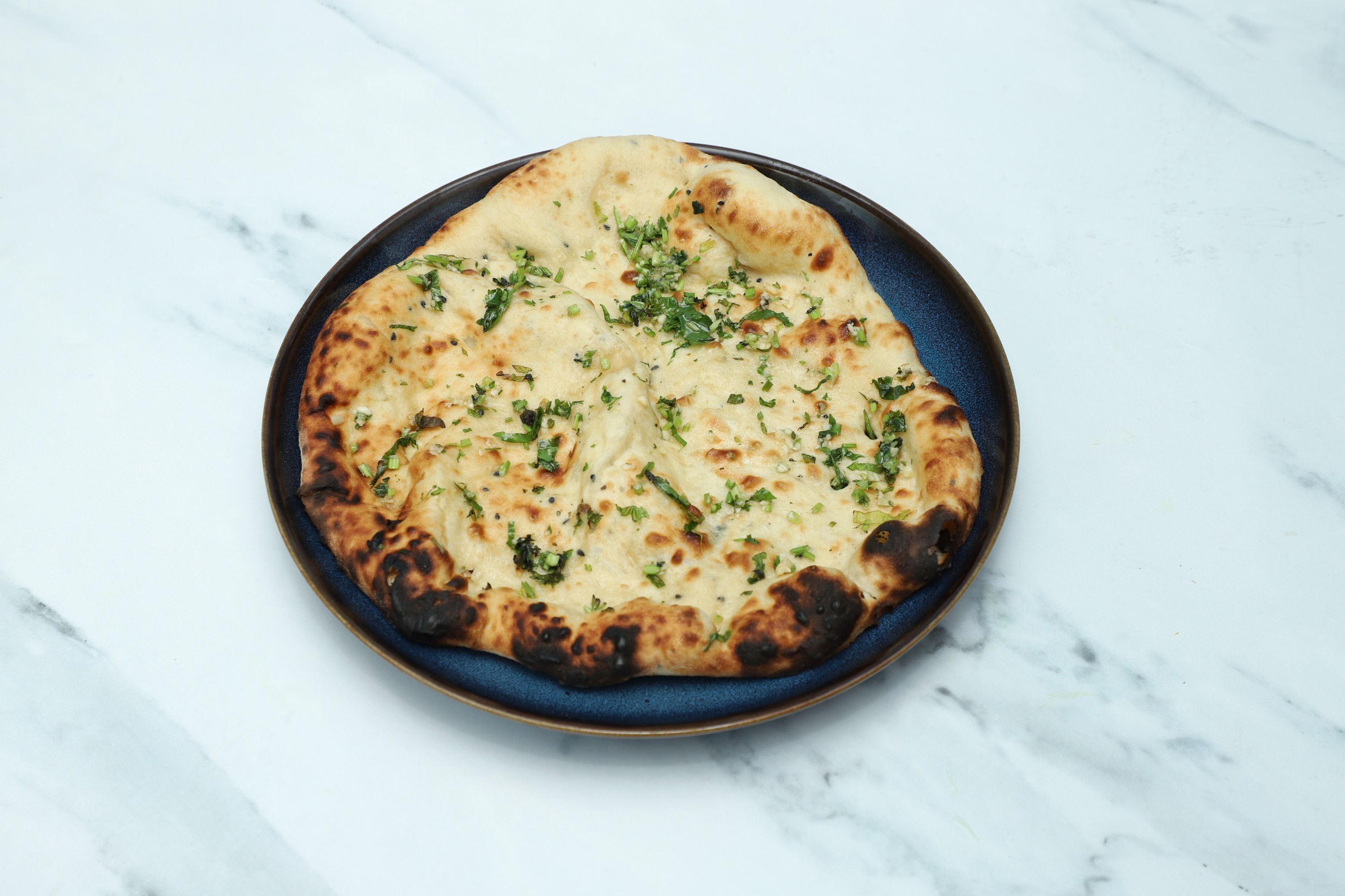 A golden-brown naan bread topped with fresh chopped garlic and coriander, served on a blue plate.