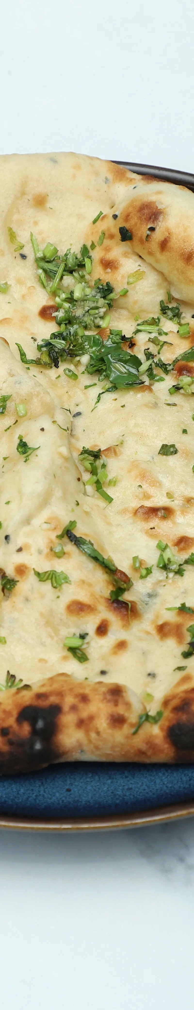 A golden-brown naan bread topped with fresh chopped garlic and coriander, served on a blue plate.