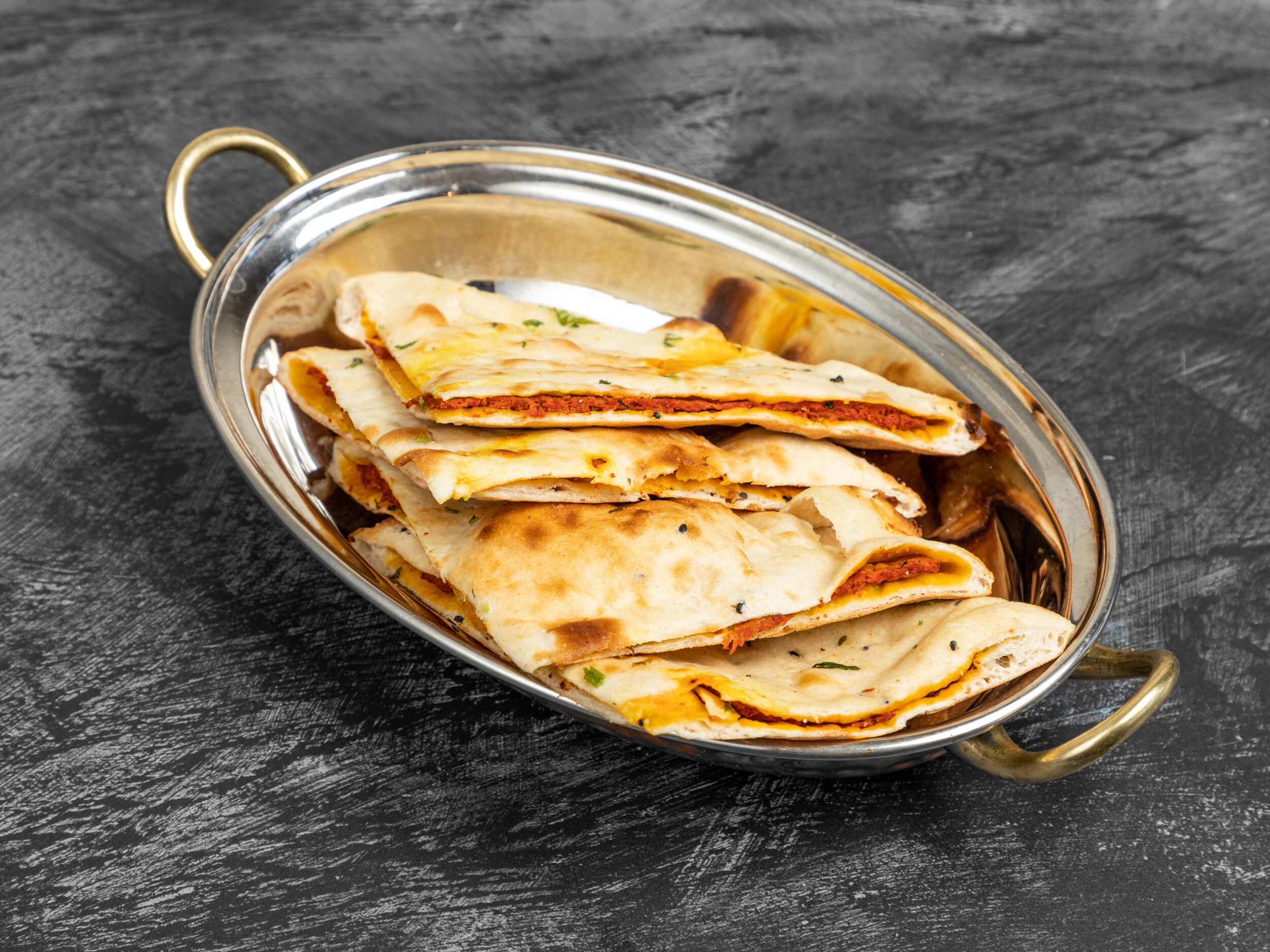 Triangular portions of stuffed naan bread with a reddish filling in a metal serving dish.