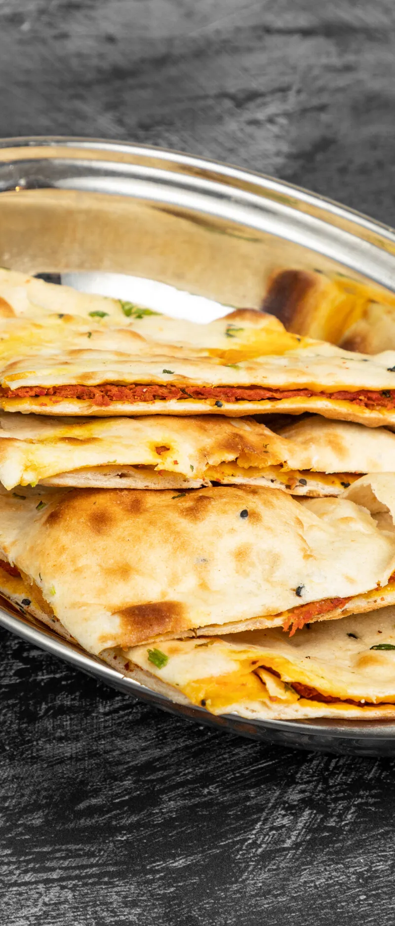 Triangular portions of stuffed naan bread with a reddish filling in a metal serving dish.
