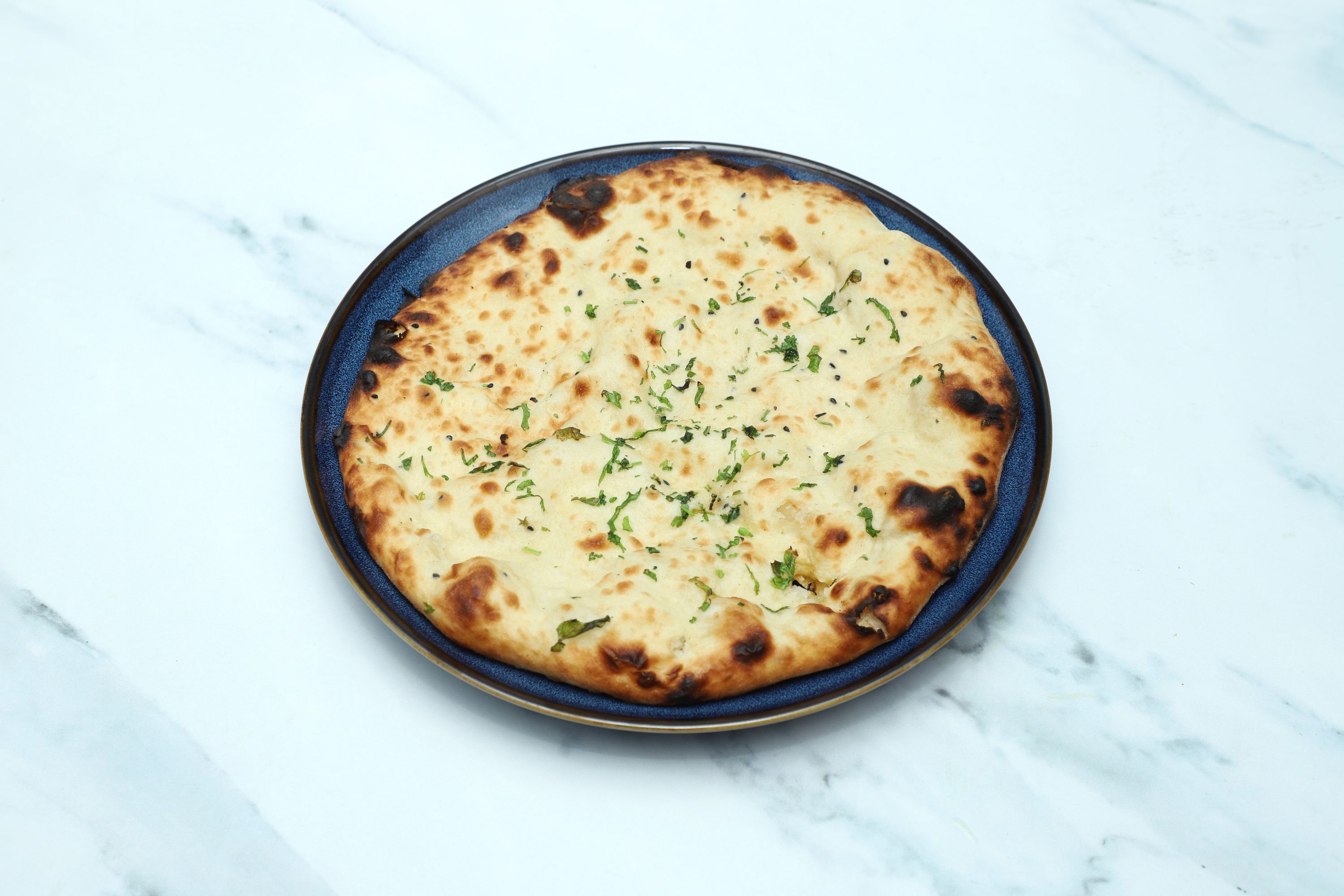 Round naan bread garnished with chopped green herbs served on a dark blue plate
