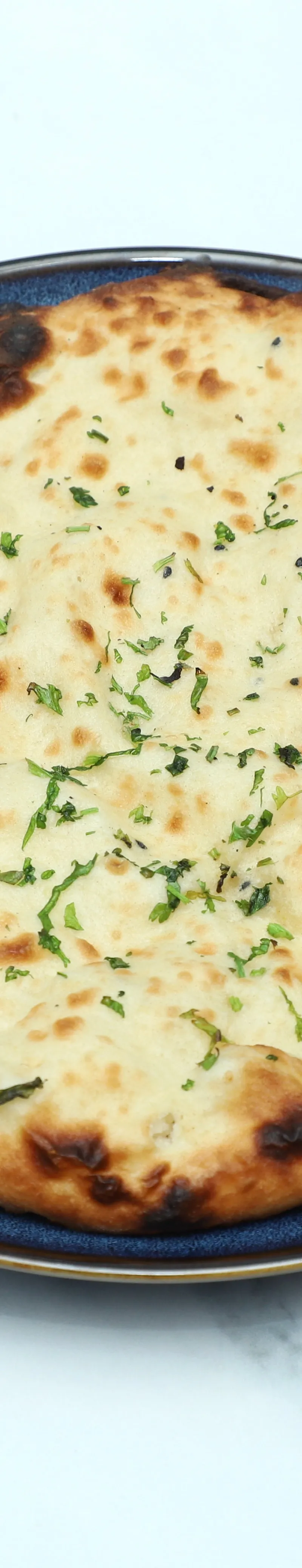 Round naan bread garnished with chopped green herbs served on a dark blue plate