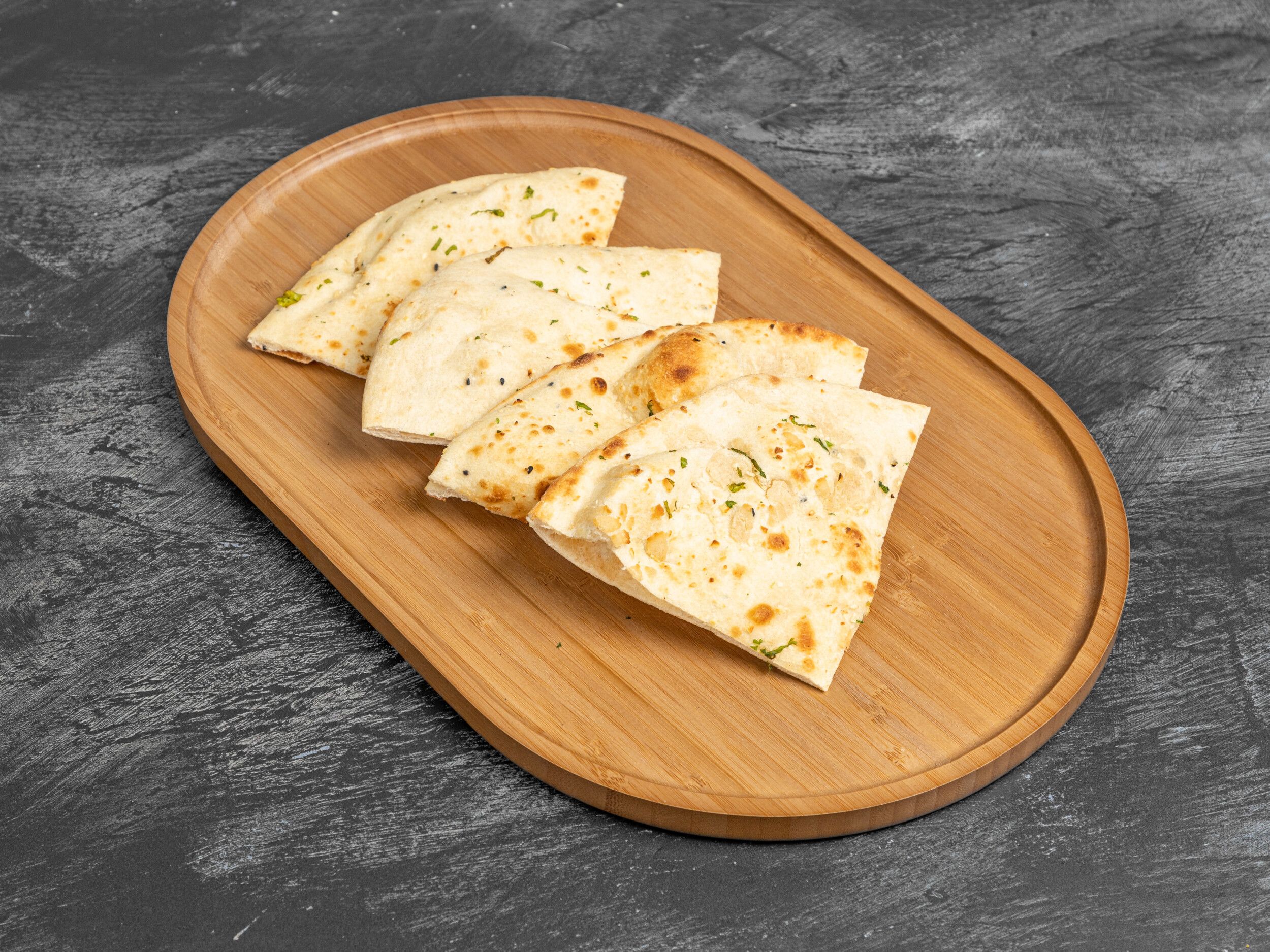 Triangular pieces of naan bread, some topped with herbs, arranged on a natural wooden serving platter.