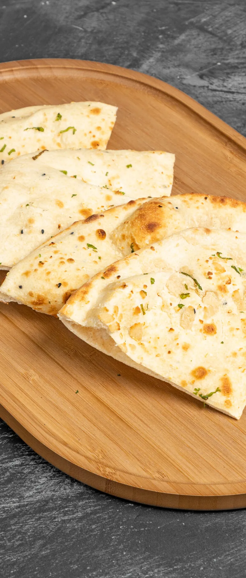 Triangular pieces of naan bread, some topped with herbs, arranged on a natural wooden serving platter.