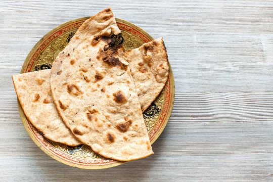 Three pieces of freshly baked naan bread with light charring on an ornate gold and red plate.