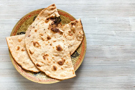 Three pieces of freshly baked naan bread with light charring on an ornate gold and red plate.