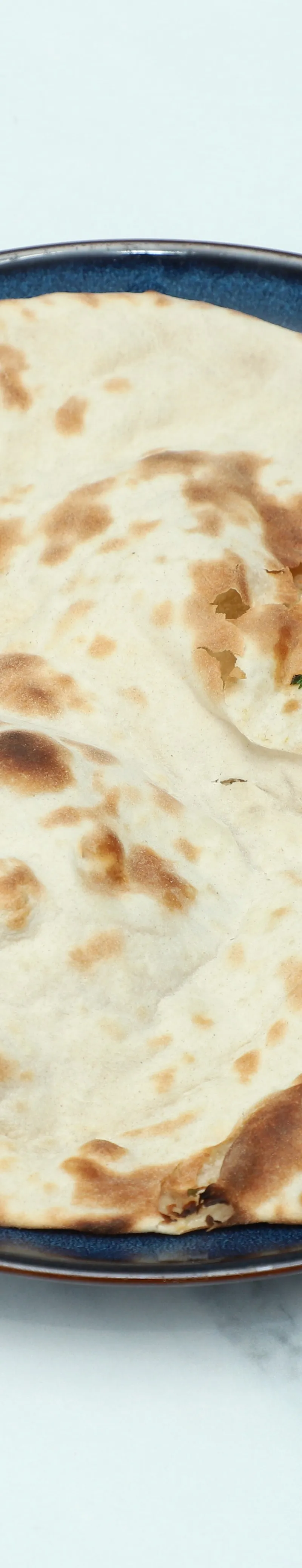 Round, golden-brown naan bread with slight charring, served on a dark blue plate on a marble surface.