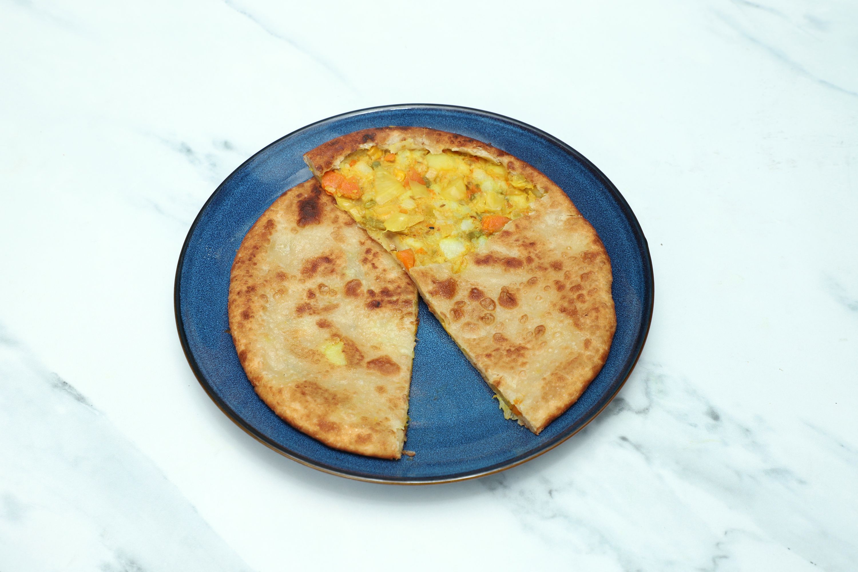 A round, golden-brown paratha with a slice cut out, revealing a colorful vegetable filling on a blue plate.