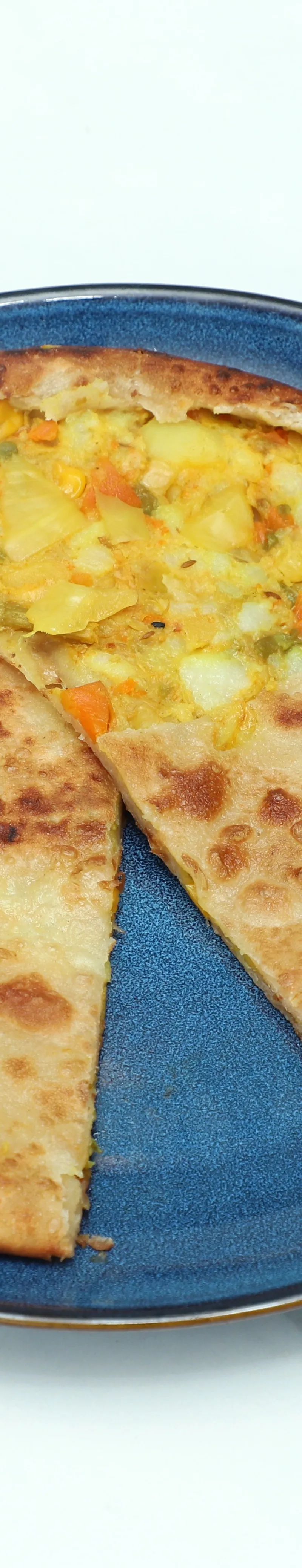 A round, golden-brown paratha with a slice cut out, revealing a colorful vegetable filling on a blue plate.