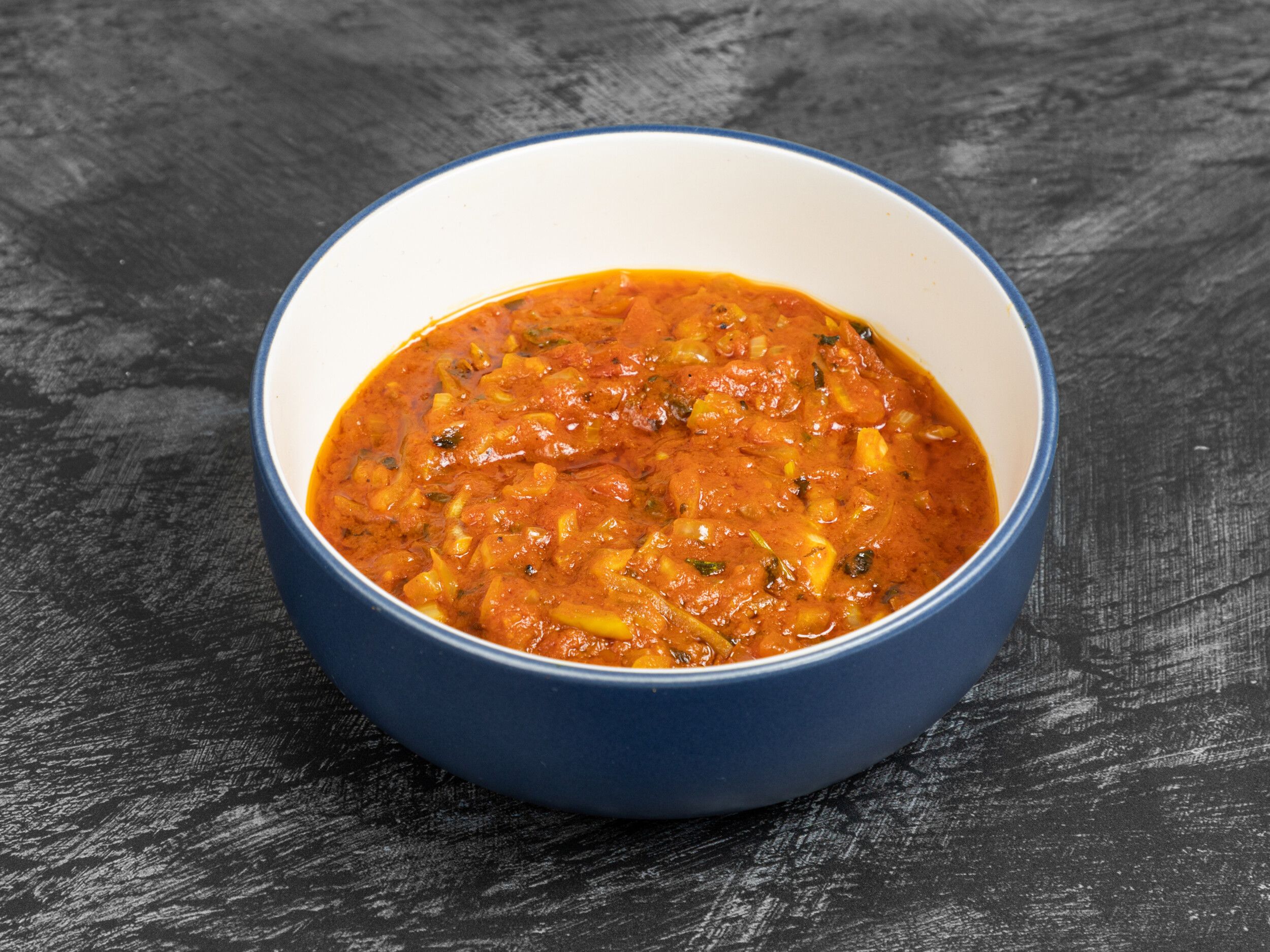 A close-up of a blue and white bowl filled with a red-orange curry sauce with chopped onions