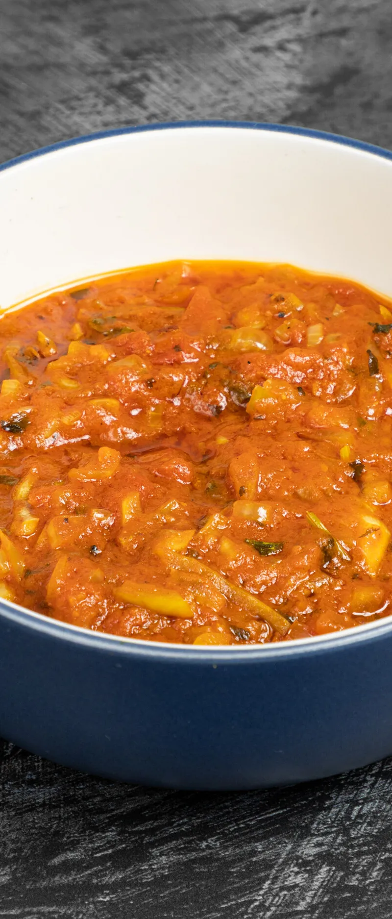 A close-up of a blue and white bowl filled with a red-orange curry sauce with chopped onions
