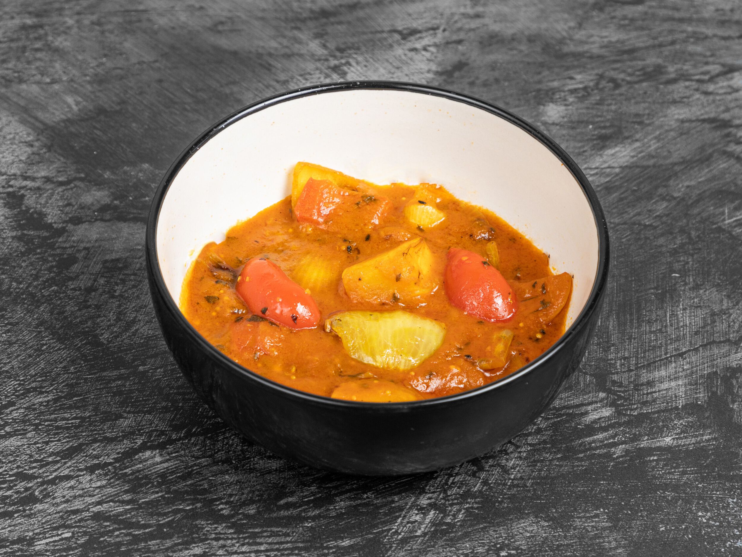 Indian-style potato and bell pepper curry with an orange sauce in a black bowl.