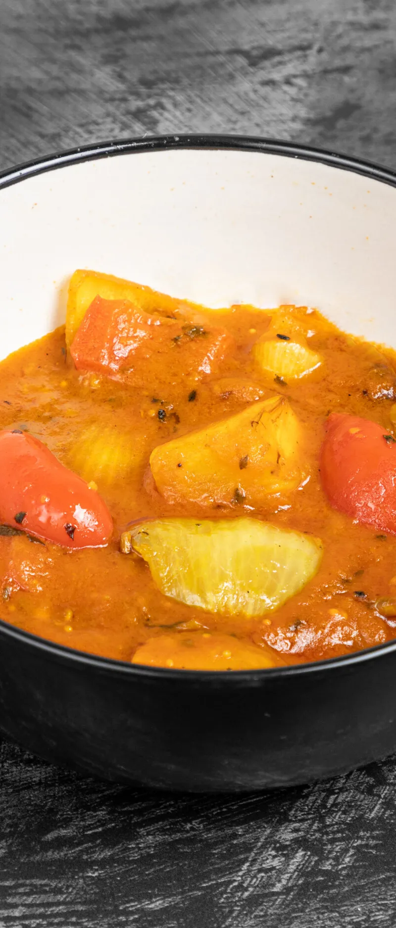Indian-style potato and bell pepper curry with an orange sauce in a black bowl.