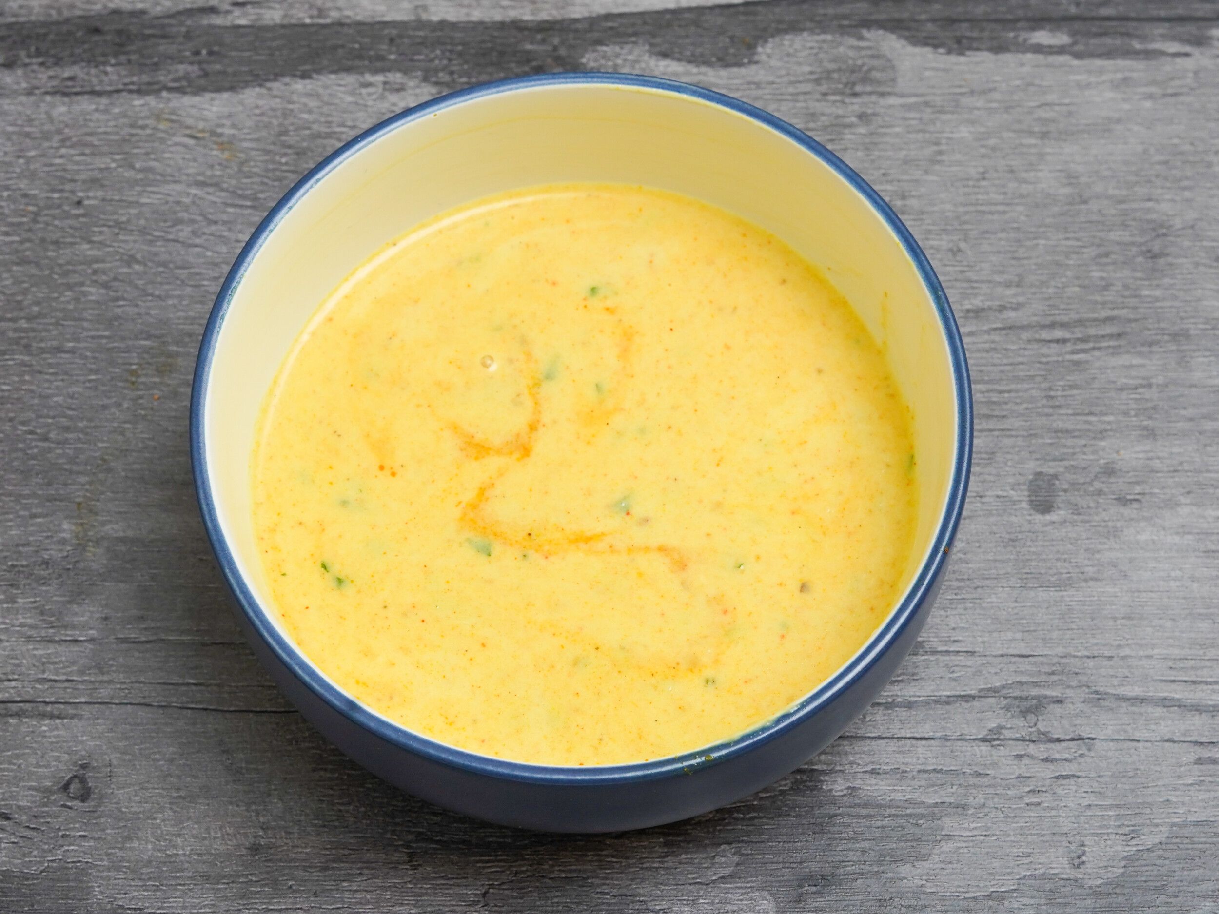 Round, blue and yellow bowl holding a creamy yellow curry or lentil dish speckled with herbs and spices.
